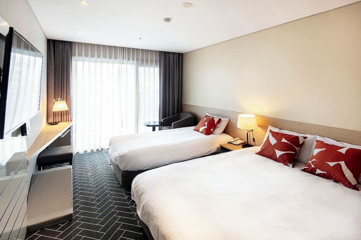 A hotel room with two beds, a desk, a chair, a TV, and a window with curtains.