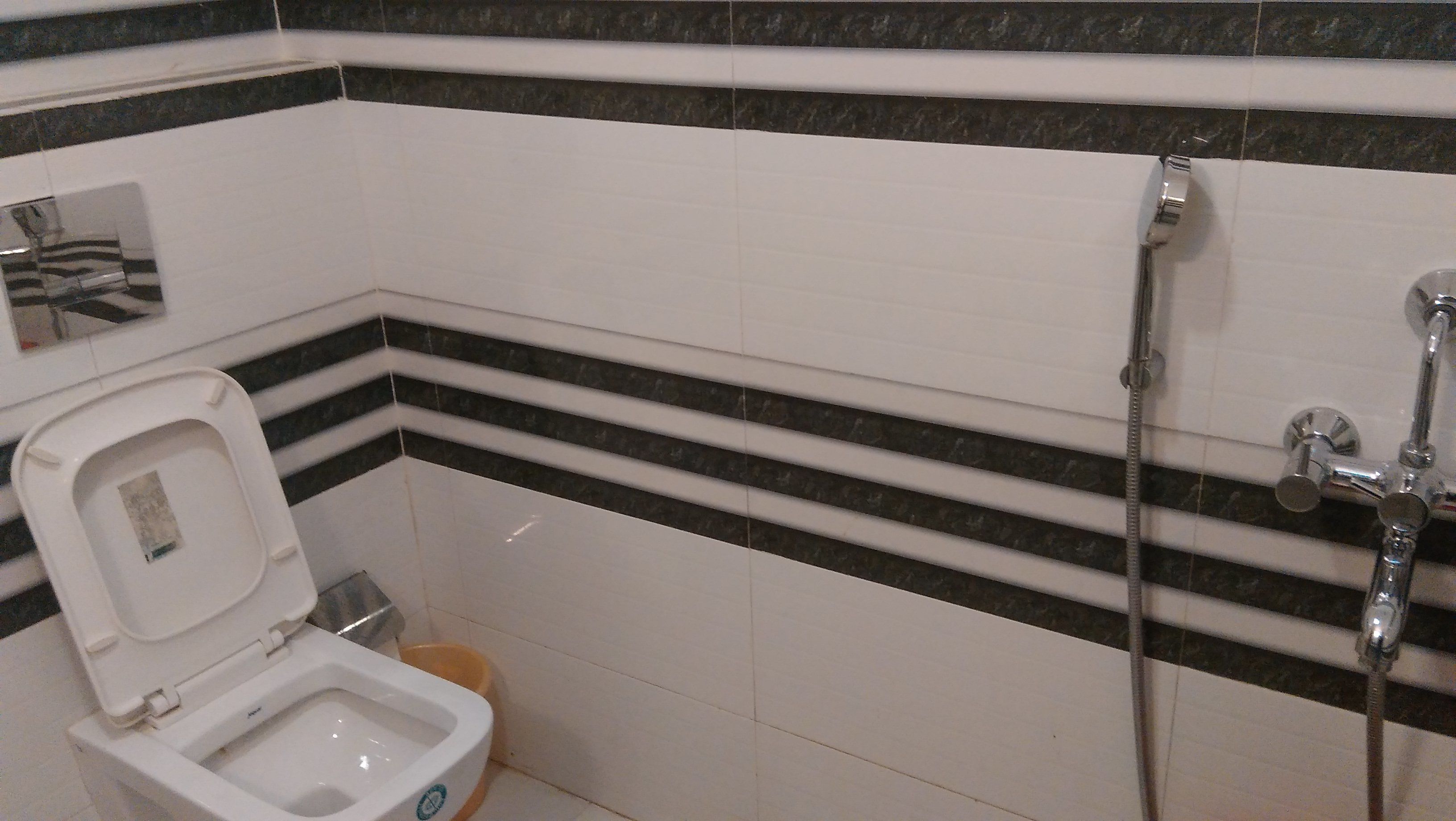Un baño con inodoro, ducha y pared de azulejos a rayas blancas y negras.
