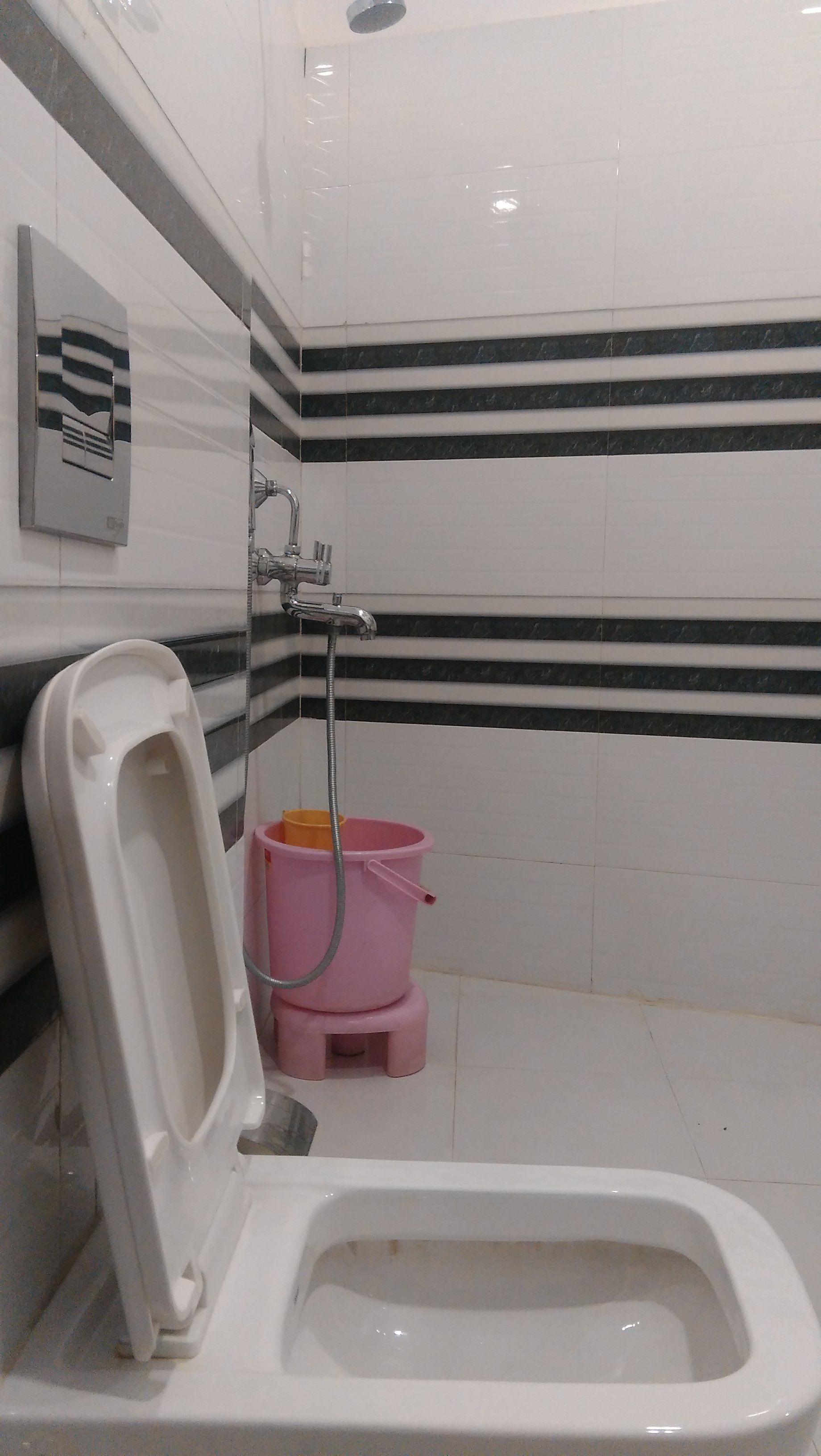 Inodoro blanco con asiento elevado, un cubo rosa y un tirador de la tapa del inodoro fijado a la pared.
