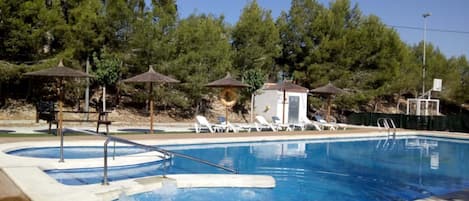 Una piscina al aire libre, sombrillas, sillones reclinables de piscina