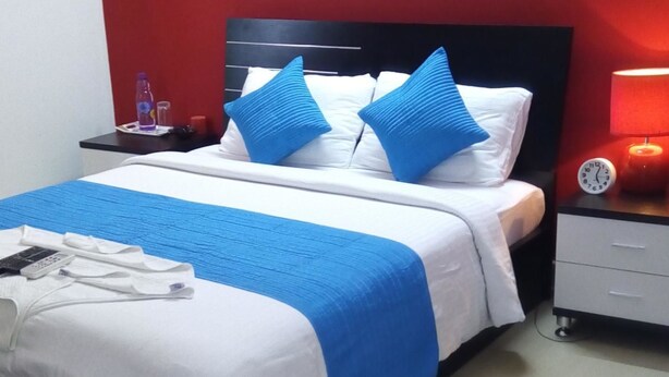 Ein Hotelzimmer mit Bett, Nachttisch, Lampe und Uhr.