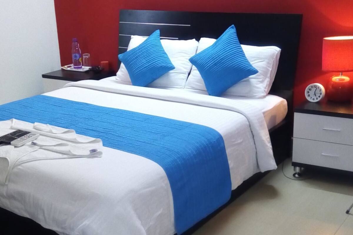 Ein Hotelzimmer mit Bett, Nachttisch, Lampe und Uhr.
