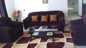 Ein Wohnzimmer mit einem dunkelbraunen Sofa, zwei Sesseln, einem Glastisch und einem gemusterten Teppich.
