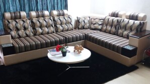 Ein modulares Sofa mit Muster, ein kleiner runder Couchtisch mit Pflanze und Figur, sowie ein dunkler Teppich.