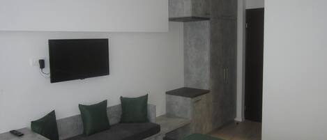 A modern bedroom with a bed, a seating area with cushions, a television mounted on the wall, and a wardrobe.