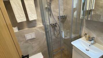 Uma casa de banho moderna com chuveiro em cabine de vidro, lavatório branco e sanita.