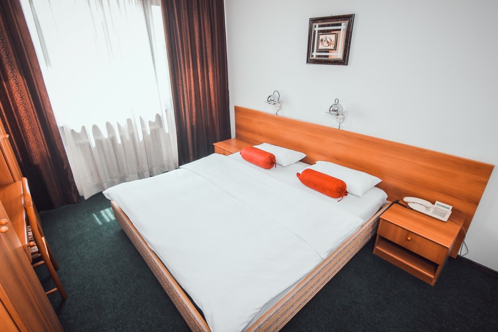 Een hotelkamer met een groot bed, een houten hoofdbord, een nachtkastje met een telefoon en een aan de muur hangend schilderij.