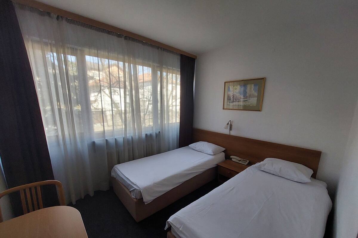 Ein Hotelzimmer mit zwei Einzelbetten, einem Holzbett, einem Schreibtisch, einem Telefon und einem Bild an der Wand.