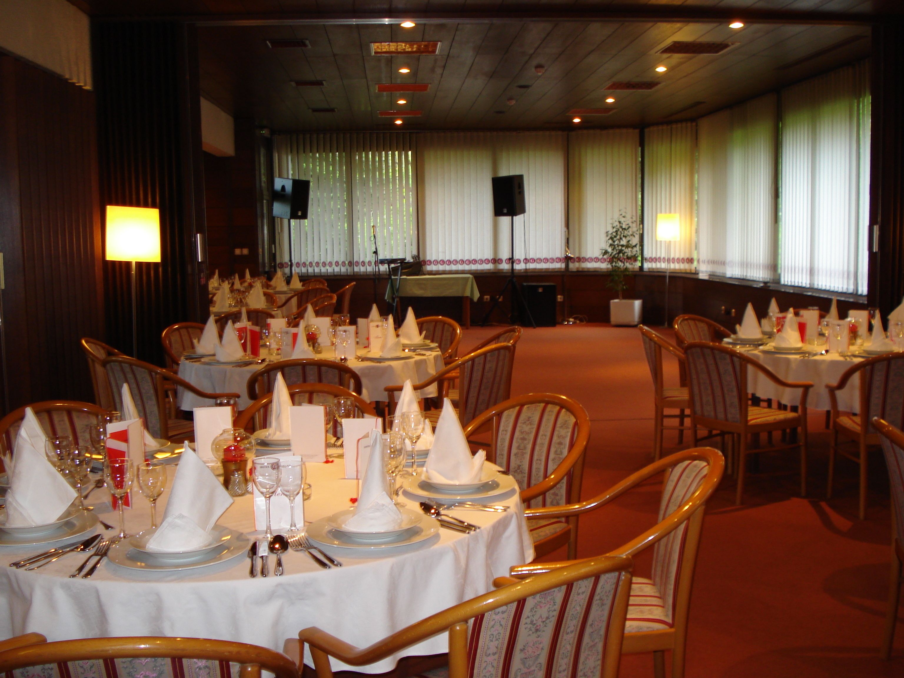 Un restaurant avec de nombreuses tables dressées pour le service, des chaises en bois et une scène en arrière-plan.