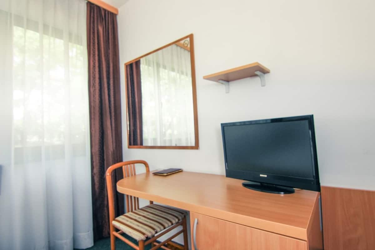 Ein Zimmer mit einem Holztisch, einem Stuhl, einem Fernseher, einem Spiegel und einem Vorhangfenster.