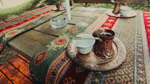 A wooden table with a patterned tablecloth, a metal tray with a cup and a pot, and a glass of water. - Hotel Grand (Sarajevo)