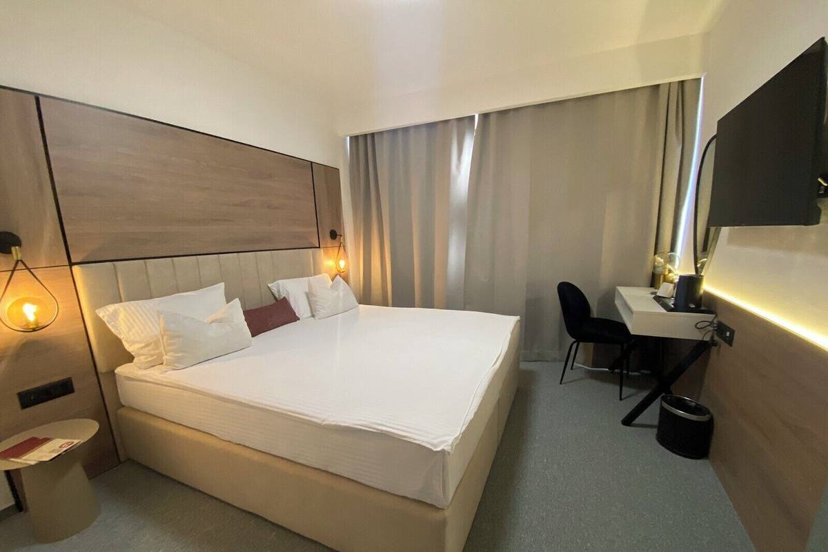 Ein Hotelzimmer mit einem großen Bett, einem Schreibtisch, einem Sessel, einem kleinen Tisch und einem Spiegel.