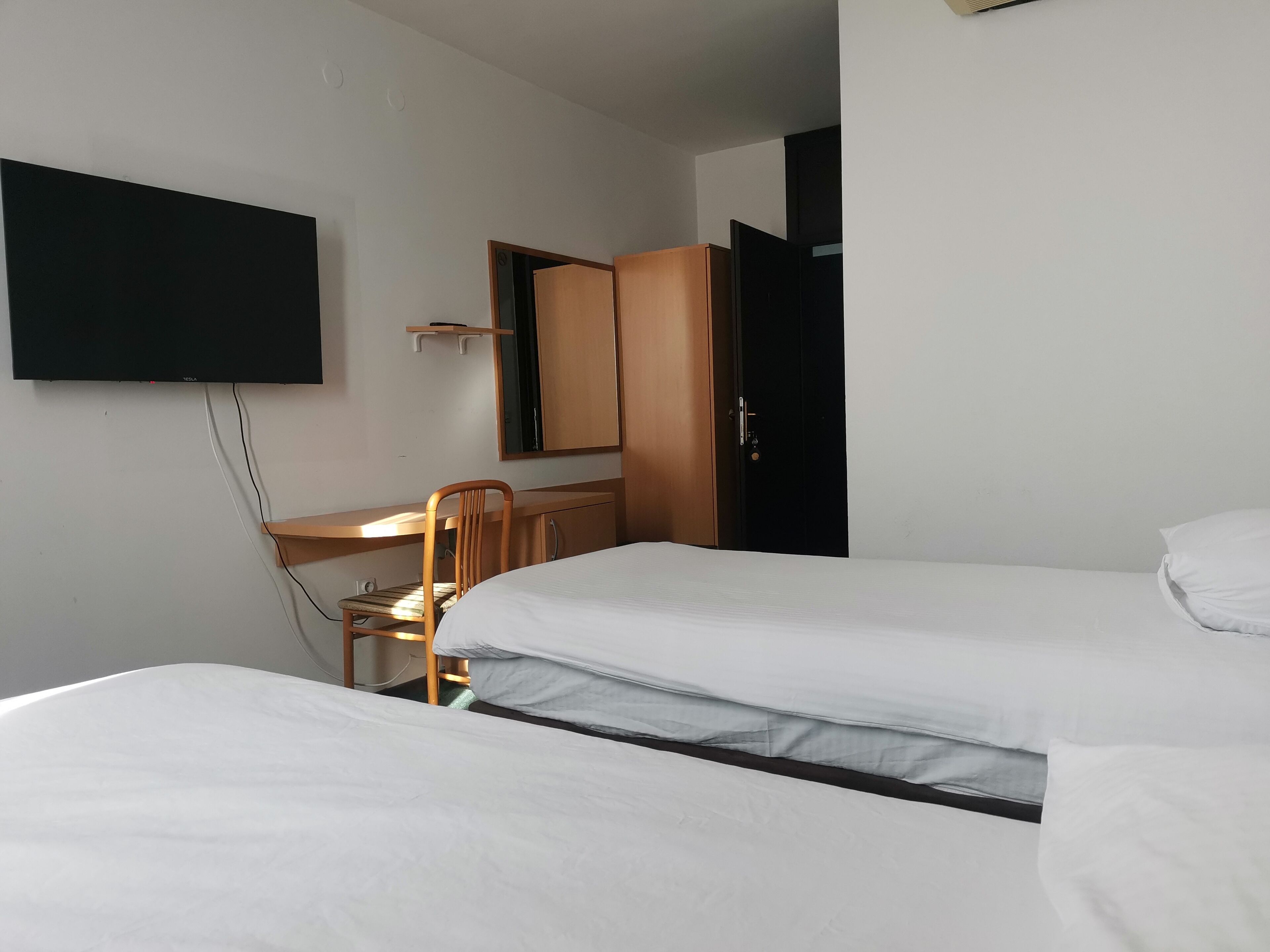 Een hotelkamer met twee bedden, een bureau, een stoel, een aan de muur bevestigde televisie en een kledingkast.