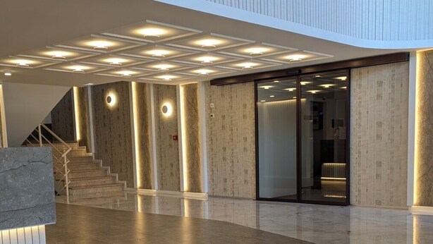 A spacious lobby with a modern design, featuring a central staircase, a reception desk, and a large glass door leading to another area. - Hotel Grand (Sarajevo)