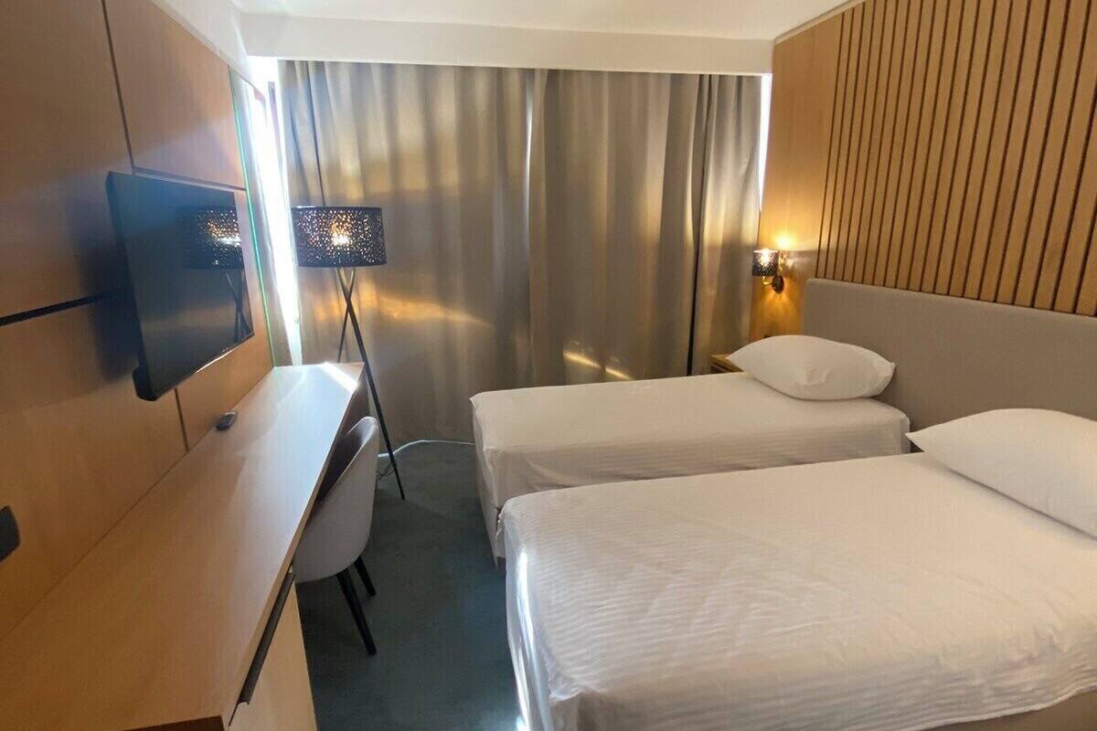 Ein Hotelzimmer mit zwei Betten, einem Schreibtisch, einem Fernseher und einer Lampe.