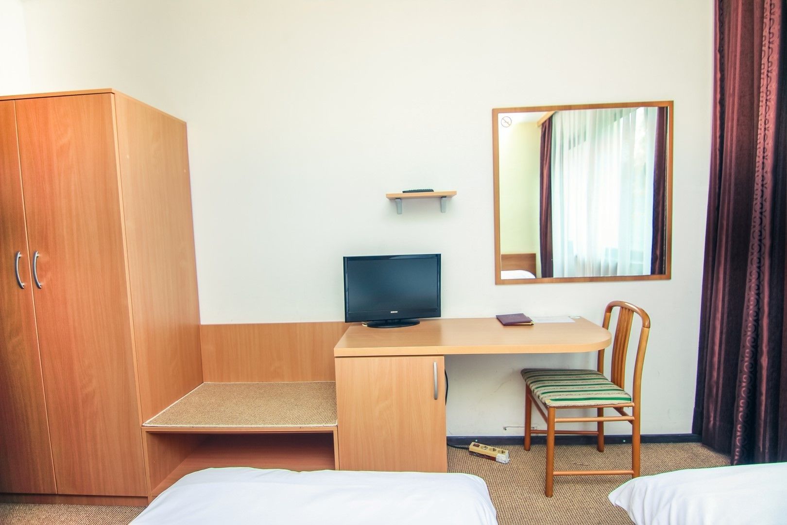 Une chambre d’hôtel avec une armoire en bois, un bureau avec un ordinateur, une chaise et un lit.