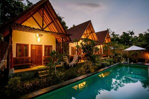 A resort with a swimming pool, wooden villas, and lush greenery. - Nuansa Penida Hostel (Penida Island)