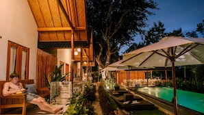 A poolside area with a wooden deck, lounge chairs, and umbrellas.