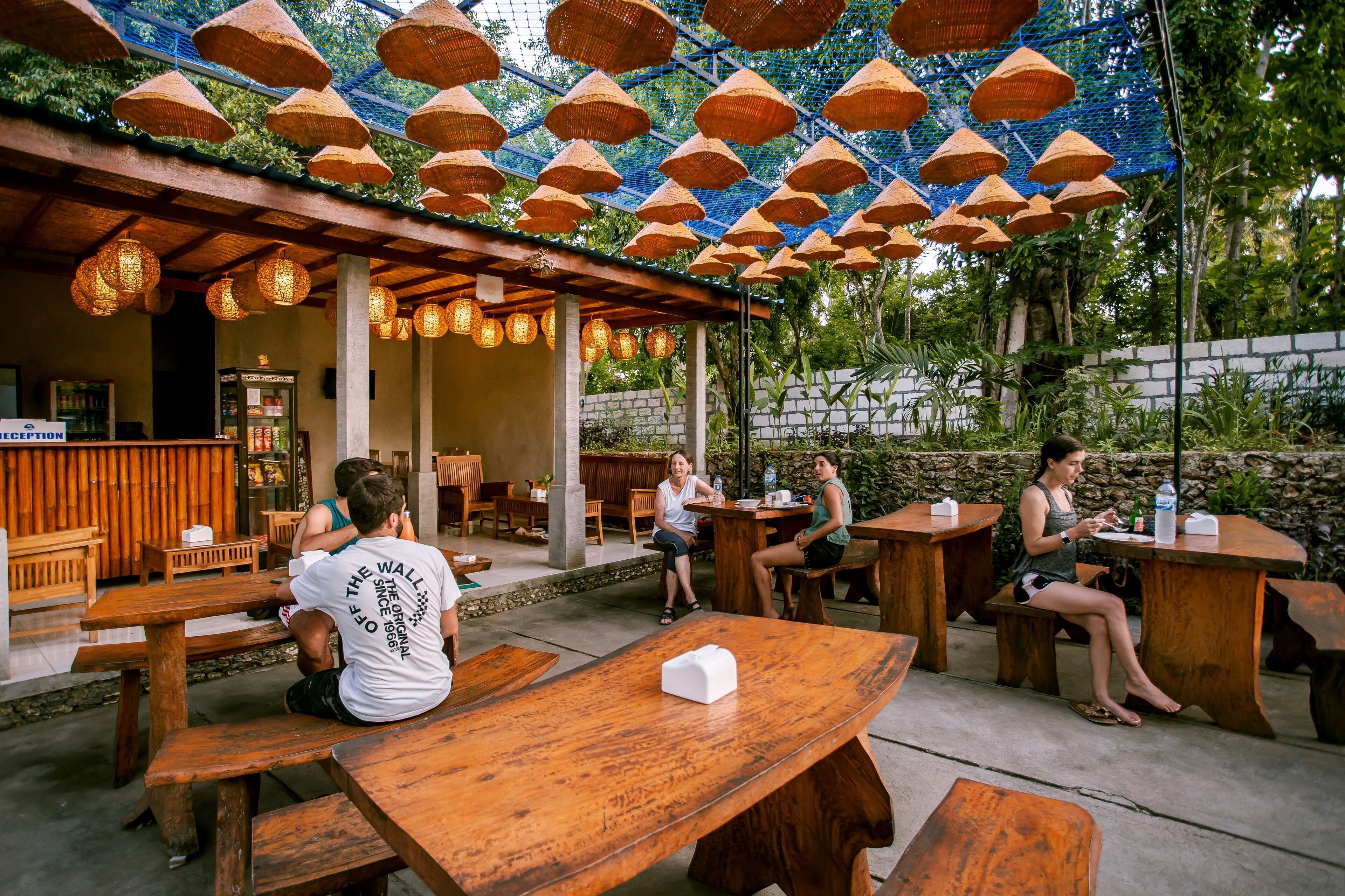 An outdoor seating area with wooden tables and chairs, a reception desk, and a covered section with hanging baskets.