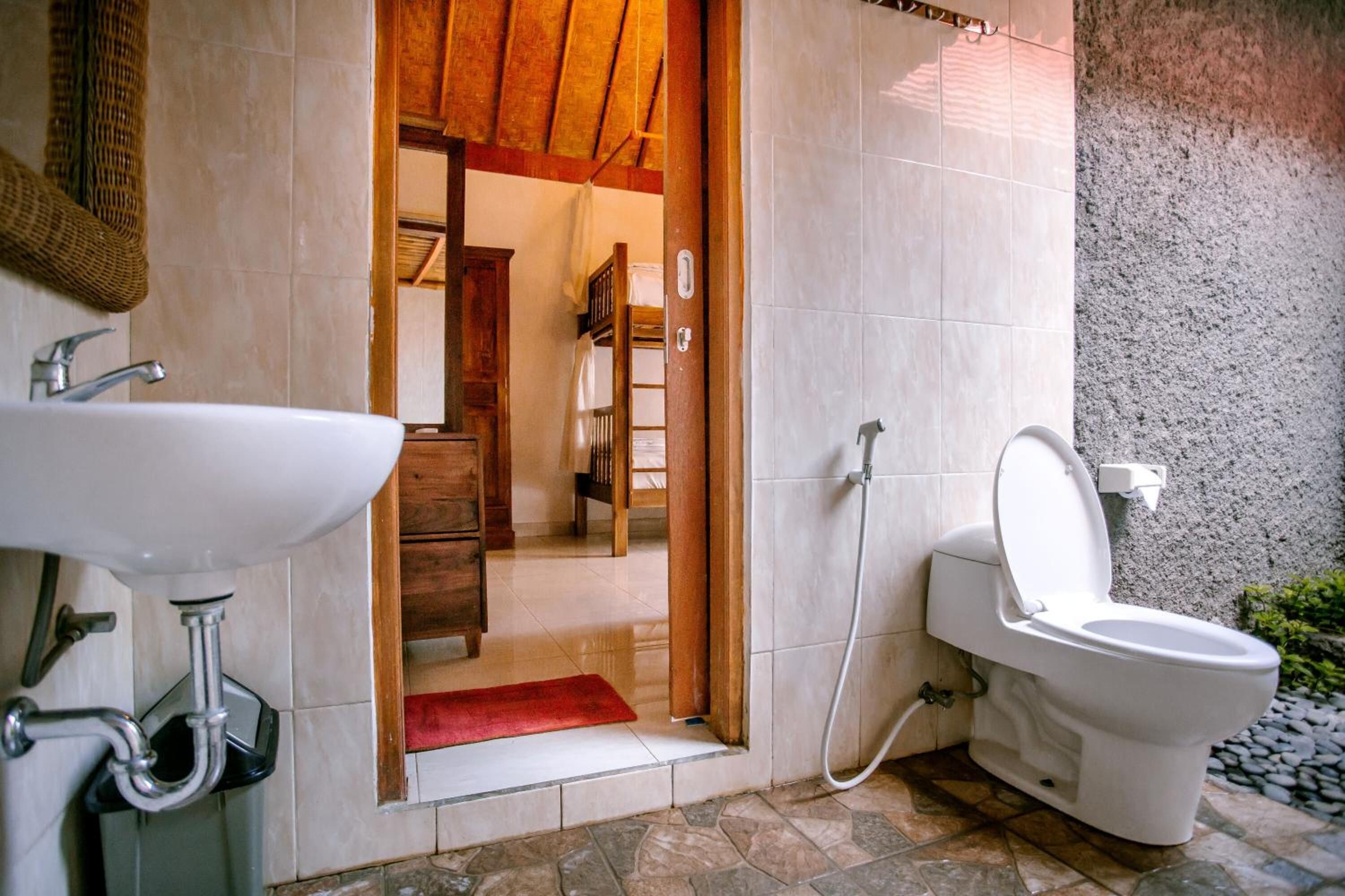 A bathroom with a white sink, toilet, and shower. There is a wooden door leading to a hallway.