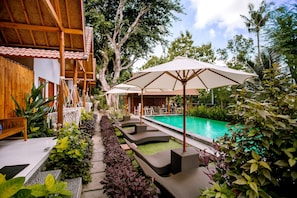Un espace piscine doté de chaises longues et de parasols, entouré d’une végétation luxuriante et d’une structure en bois.