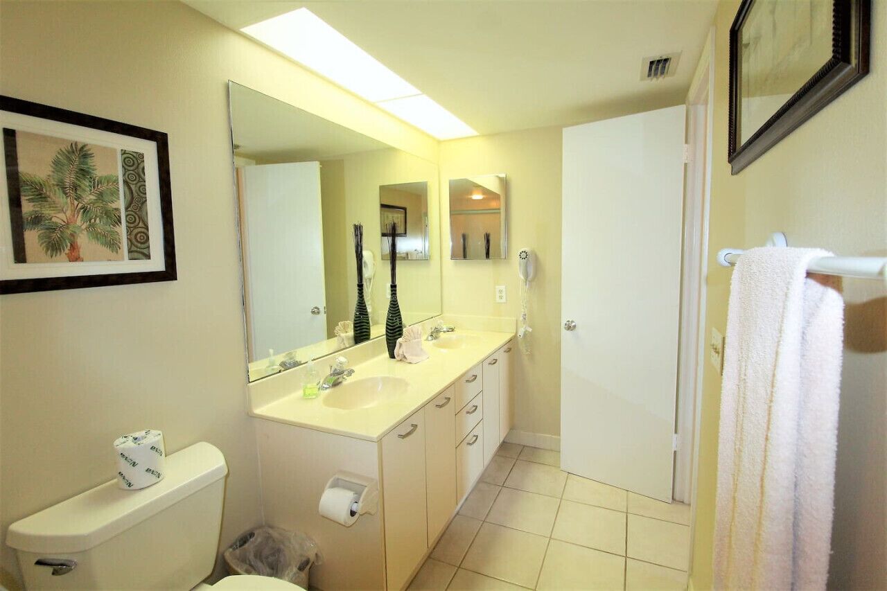 A bathroom with a toilet, sink, and mirror. There is a towel rack with a towel hanging on it.