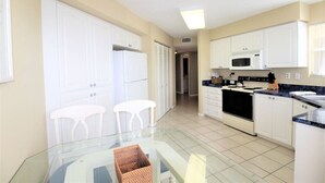 A modern kitchen with white cabinets, a microwave, stove, and a glass dining table with two chairs.
