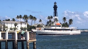 Eine Pier mit einem Holzdeck, ein weißes Gebäude mit zahlreichen Fenstern und ein großes weißes Boot mit einem roten Rettungsboot auf dem Deck.