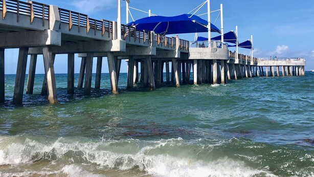 Eine Pier mit blauen Sonnensegeln und Blick auf das Meer.