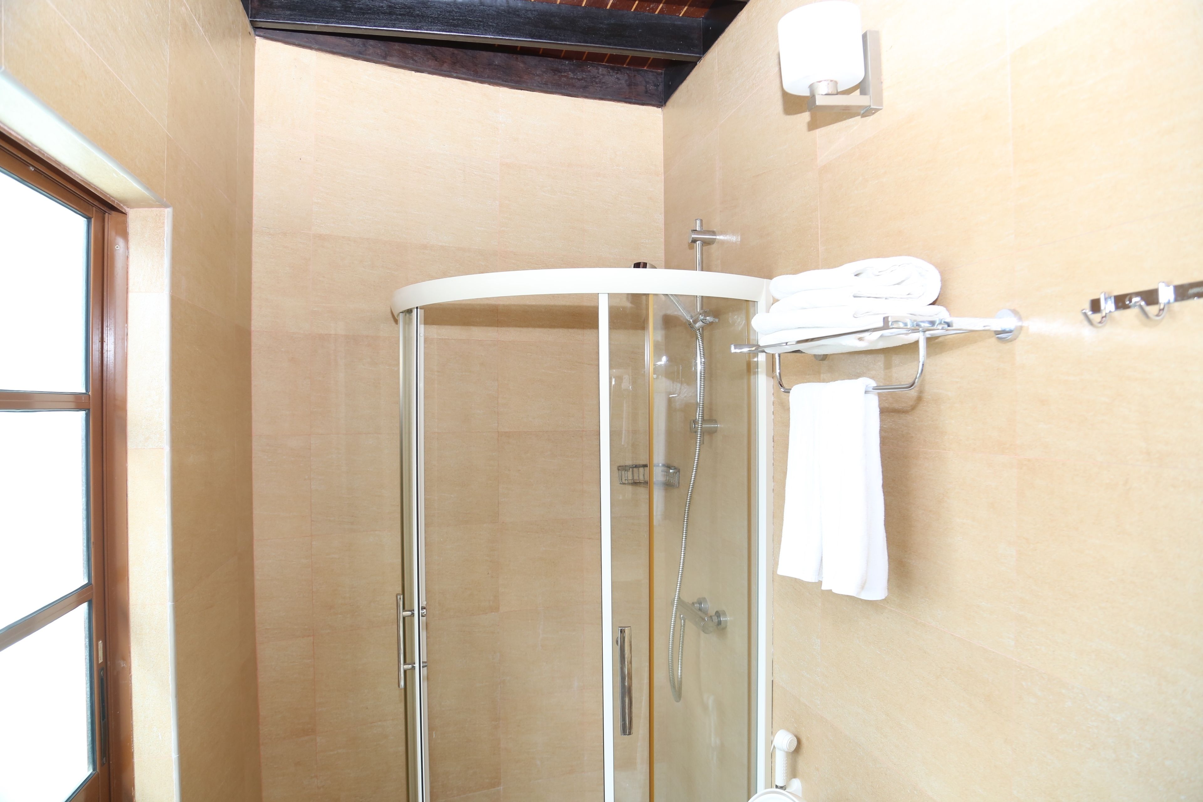 Une douche fermée par des parois en verre, avec un porte-serviettes blanc et une douchette à main.