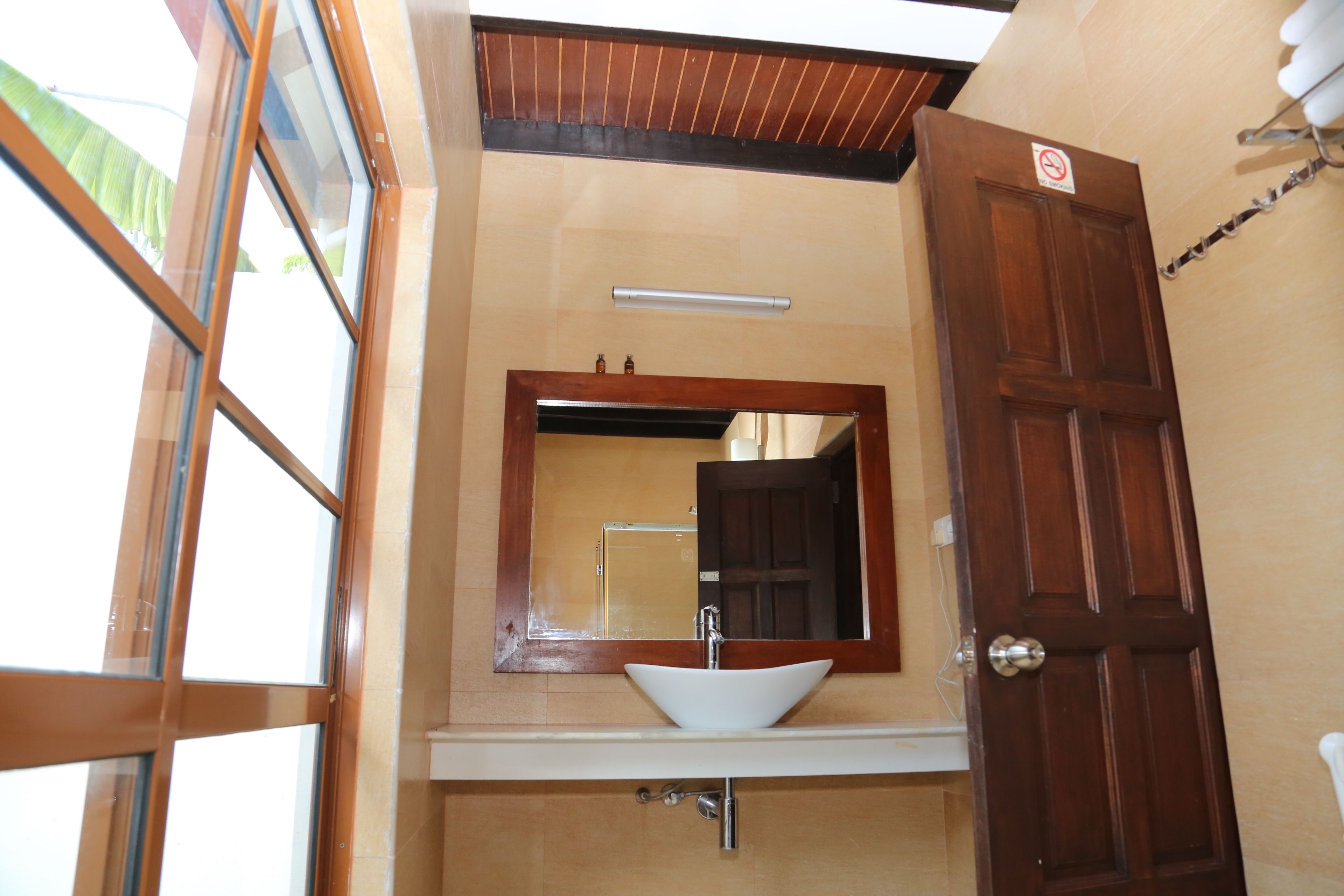 Un baño con puerta de madera, un lavamanos blanco y un espejo encima.