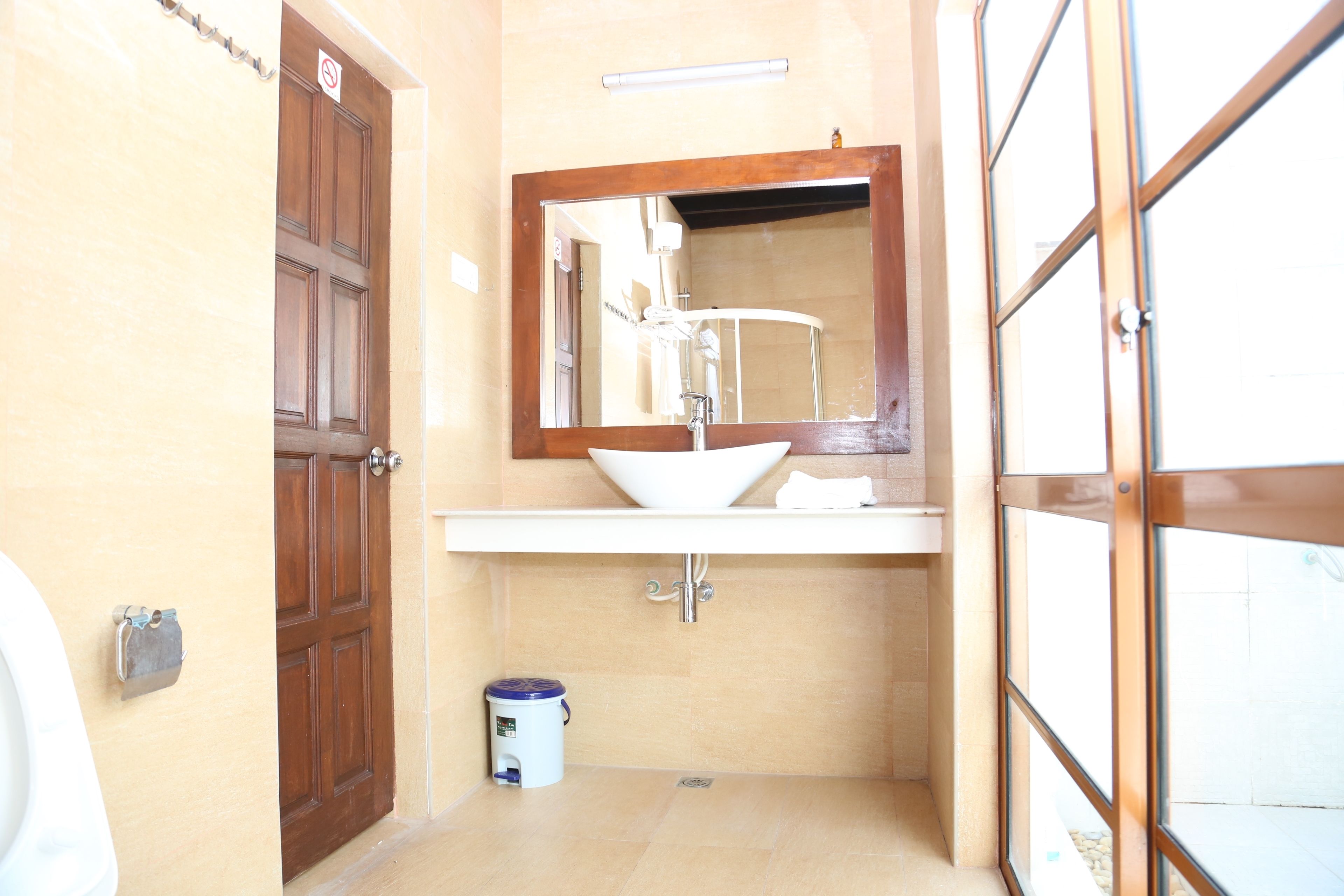 Un baño con puerta de madera, un lavabo blanco y un espejo encima.