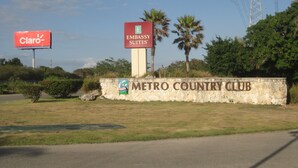 A sign for Embassy Suites and Metro Country Club with a stone wall and greenery.