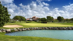 A golf course with a pond, a house in the background, and a clear sky.