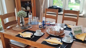 Une table à manger dressée avec des assiettes, des serviettes, des couverts et un gâteau, entourée de chaises en bois et de bancs rembourrés.