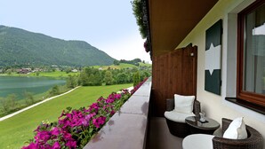 Een balkon met rieten meubilair, uitzicht op een meer en een berg op de achtergrond.