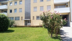 A multi-story building with a flat facade, several windows, and a small garden area with pink flowers.