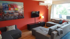 A modern living room with a red accent wall, a flat-screen TV, a sofa, a coffee table, and a chandelier.