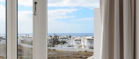 A view from a window overlooking a residential area with houses, a clear sky, and a distant body of water.