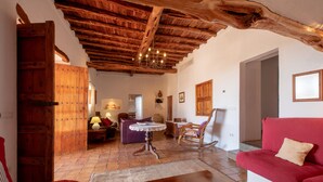 Una habitación con techo de madera, un sofá rojo, una mecedora de madera, una mesa y una puerta.