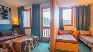 Een gezellige kamer met een bank, een klein tafeltje en een bed. Er zijn ramen met gordijnen, uitzicht op het omliggende landschap en een houten plafond.