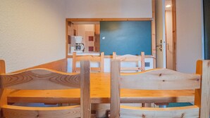 Een houten eettafel met stoelen, een koffieapparaat en een prikbord aan de muur.
