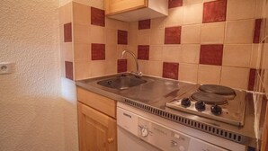 Een kleine keuken met een spoelbak, fornuis en houten keukenkastjes.