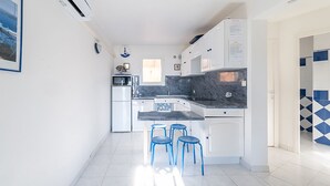 A compact kitchen with white cabinets, a marble countertop, and blue bar stools.