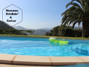A swimming pool with clear blue water, surrounded by palm trees and a mountainous landscape. - APPARTEMENT CARDU  (SAINTE LUCIE DE TALLANO)