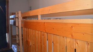 Un lit superposé avec une structure en bois et des barreaux en métal, une petite fenêtre et une porte.