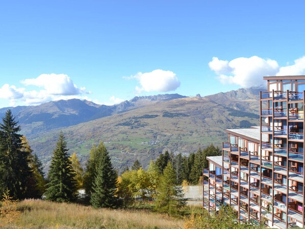 A modern multi-story building with balconies, set against a backdrop of mountains and clear skies.