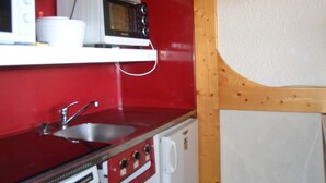 Une cuisine compacte avec un plan de travail rouge, des appareils électroménagers blancs et une structure en poutres apparentes.