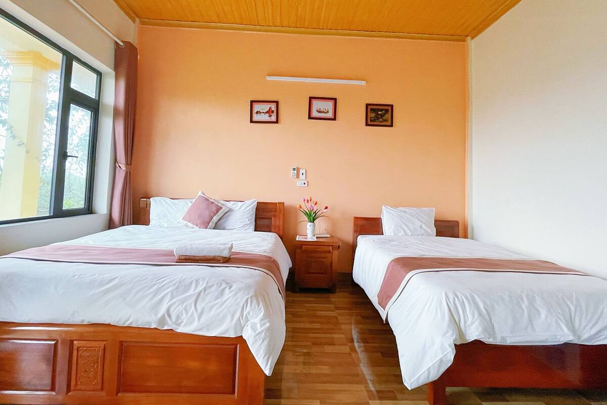 Une chambre d’hôtel avec deux lits, des têtes de lit en bois, un plancher en bois, une fenêtre avec des rideaux et un mur orné de deux tableaux encadrés.