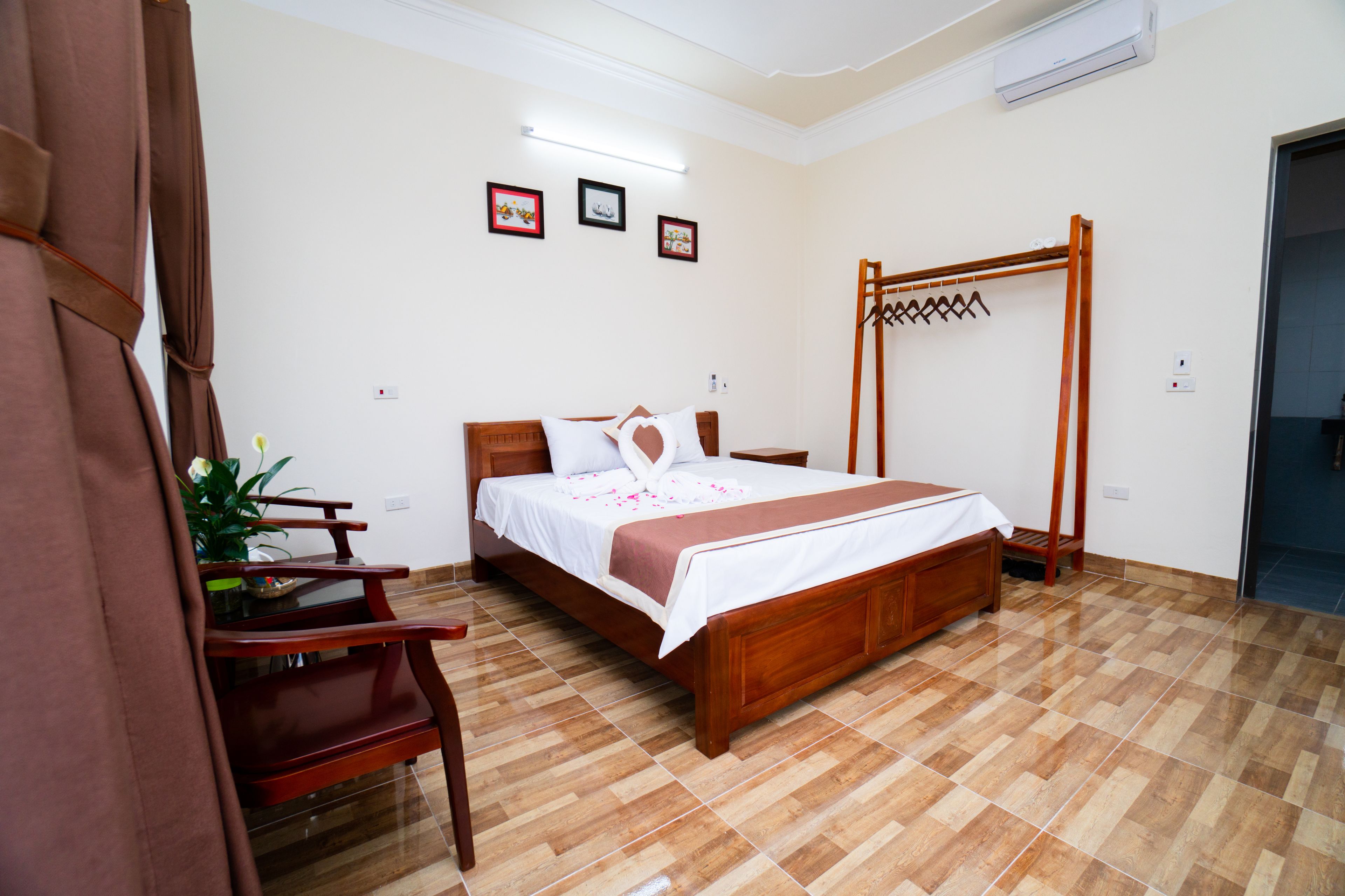 A neatly arranged bedroom with a wooden bed, a wooden chair, a small table with a plant, and a wooden drying rack.